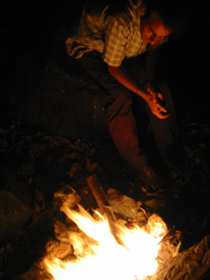a man is sitting by a campfire and looking at a phone