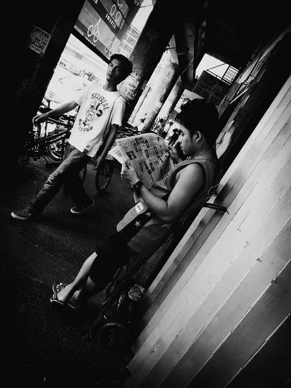 two boys are standing on the sidewalk with a news paper