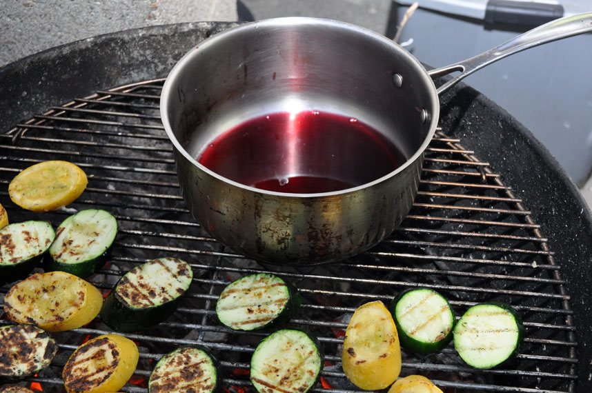 some vegetables are on the grill with food cooking on the grill