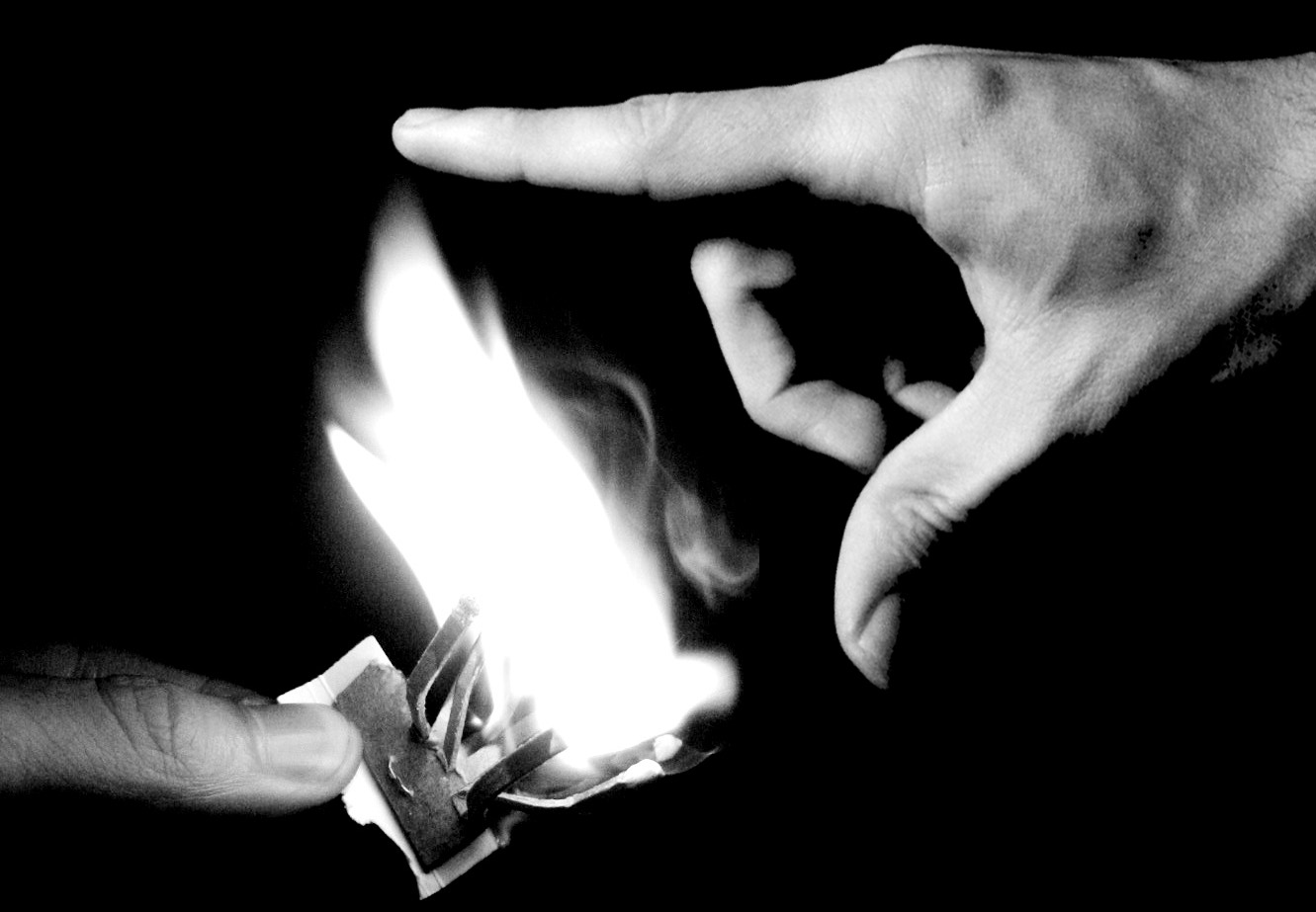 two hands are lighting a match book in the dark
