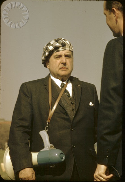 a man in suit and hat holding a device with a cord