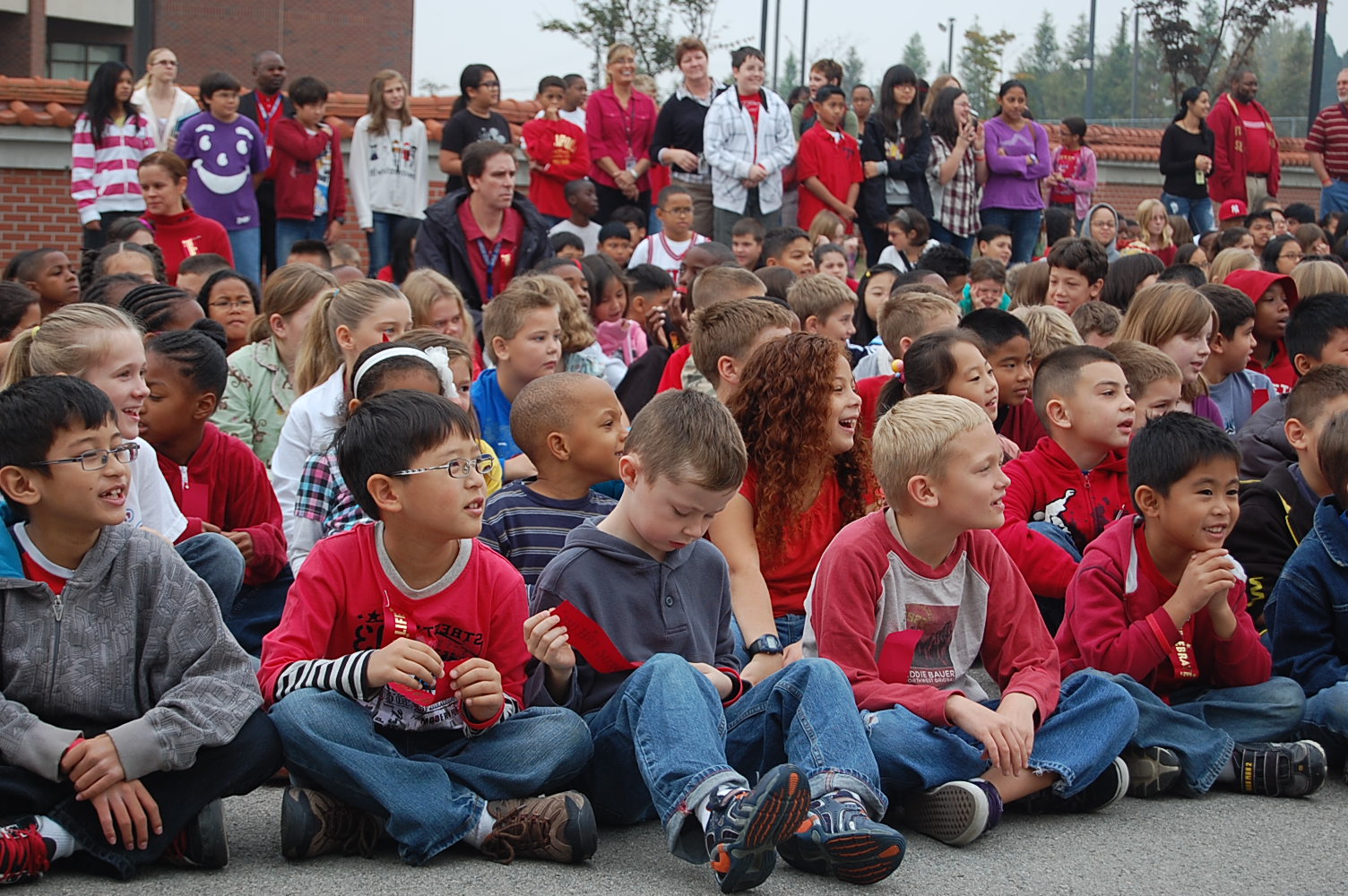 a crowd of children sitting on the ground watching soing