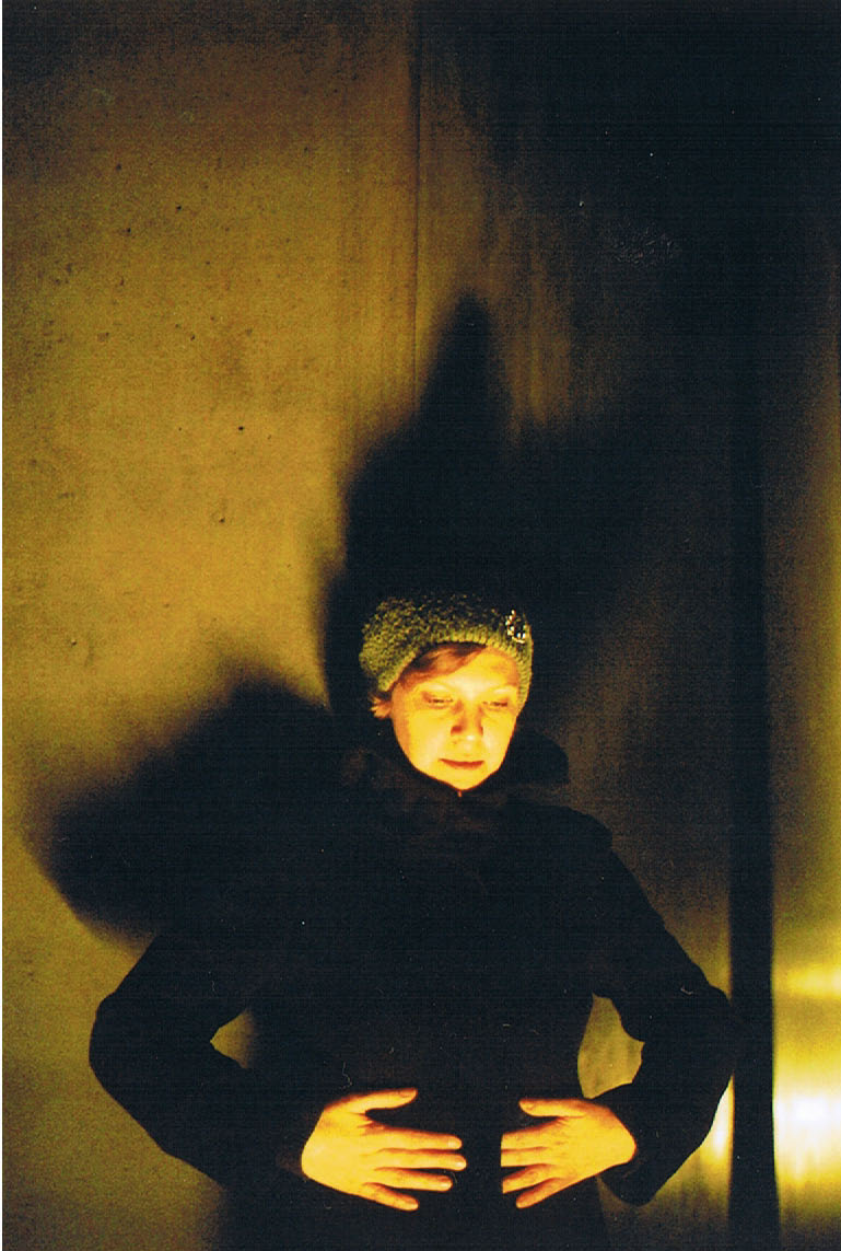 a woman poses in the shadows, against the wall