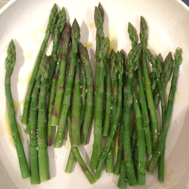 cooked asparagus spears on a white plate with oil