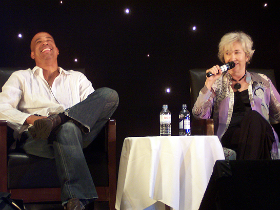 a woman sits in a chair as a man holds a microphone in his hand