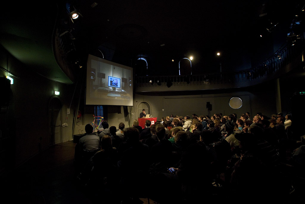 an audience watching the projection of a person on stage