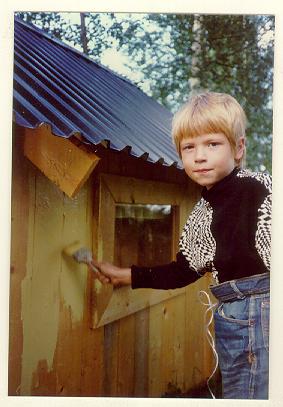 a boy standing in front of a wooden bird house