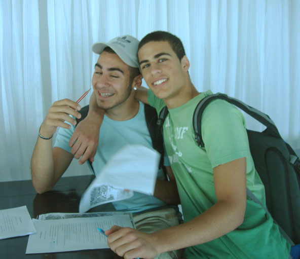 two men sitting at a desk smiling and looking in a camera