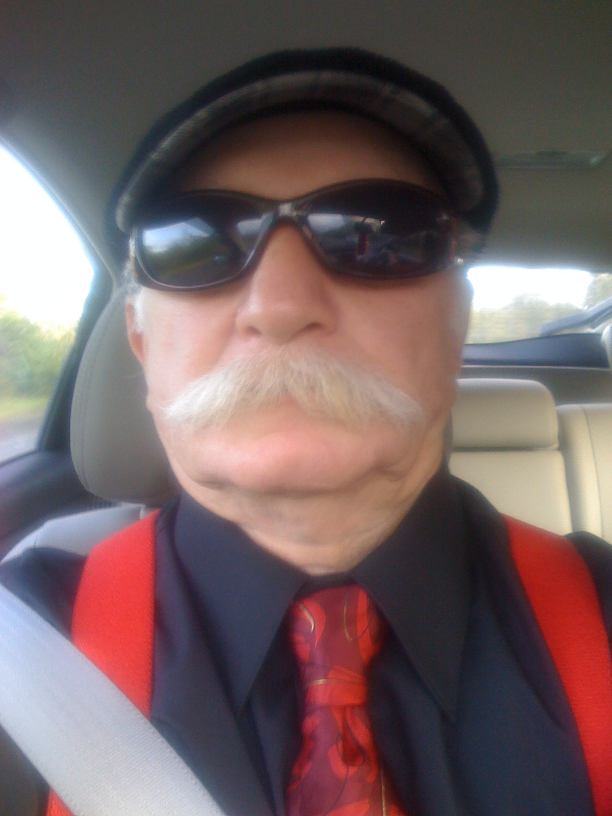 a bearded man wearing a suit and tie, driving a car