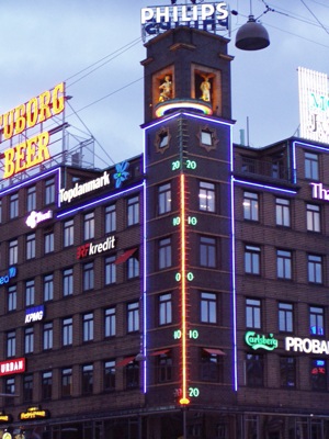 a building with a clock tower on top and neon signs over it