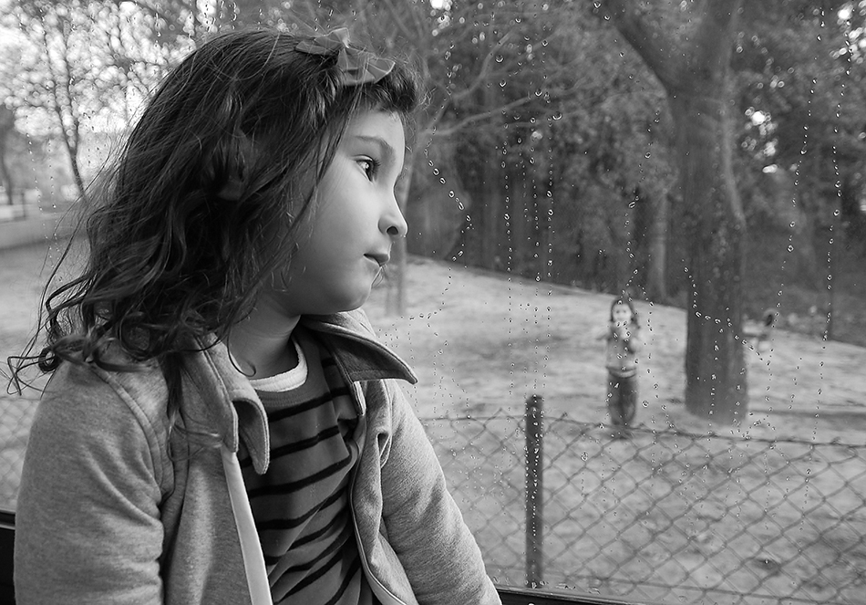 little girl stares out window with rain drops on the windowsill