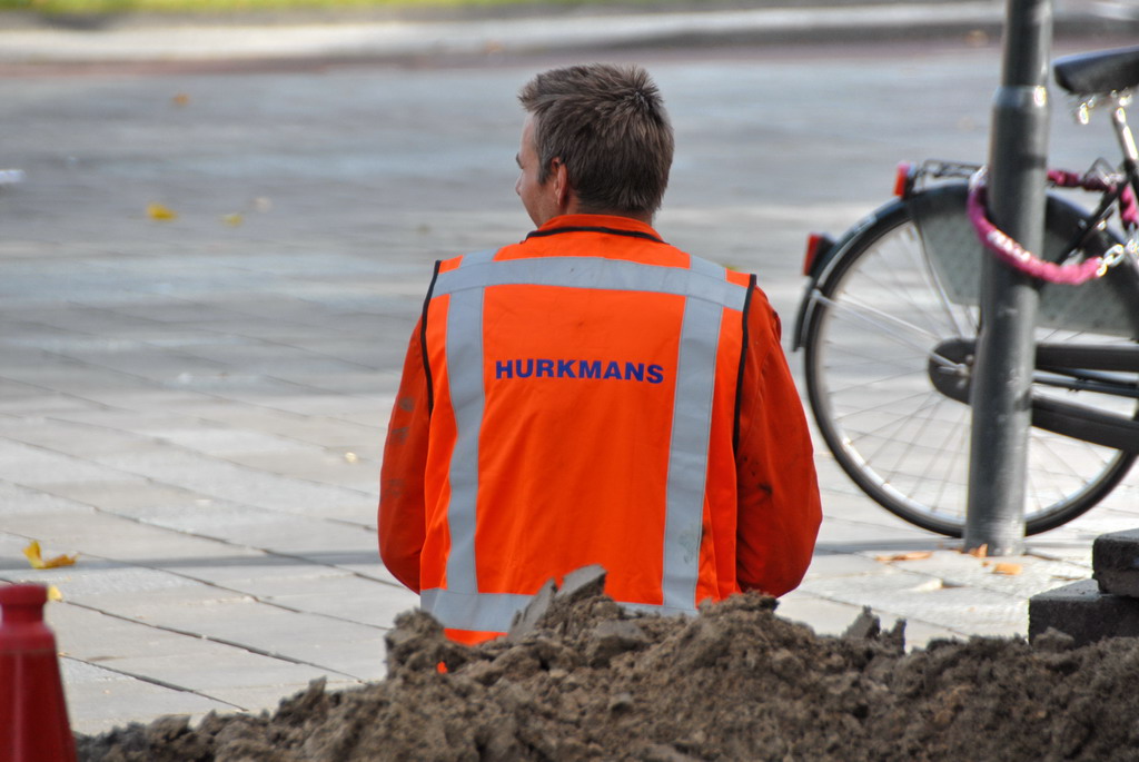 a person in orange and grey safety jacket looking at bike on street