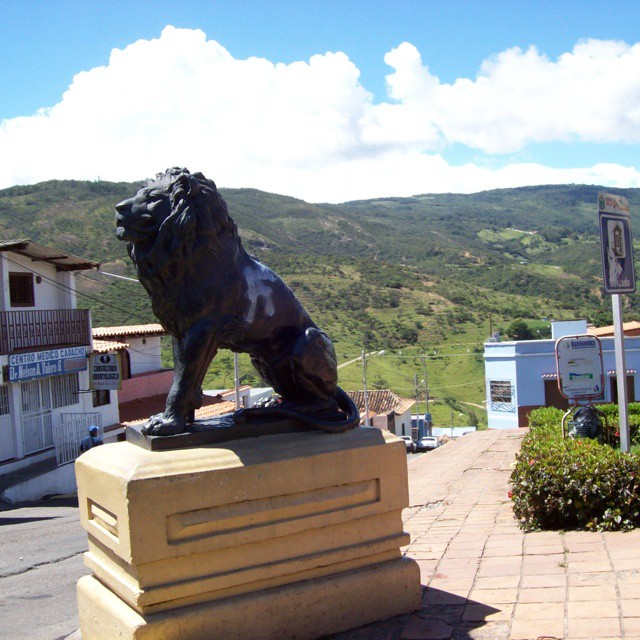 statue of a lion on a stone platform near some buildings
