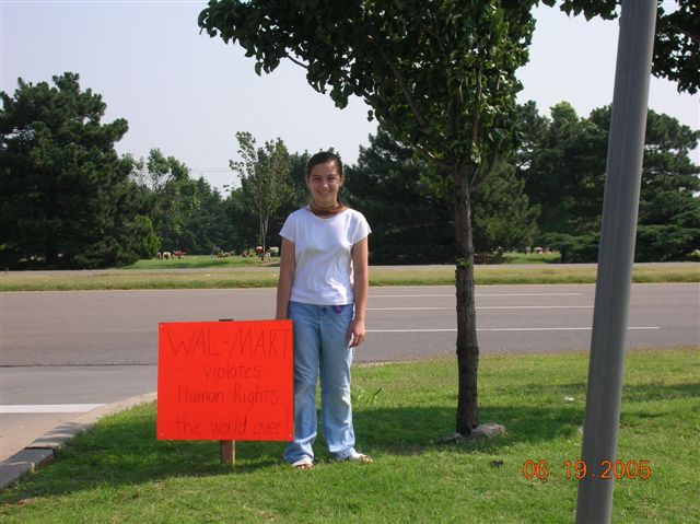a woman standing by a red sign next to trees