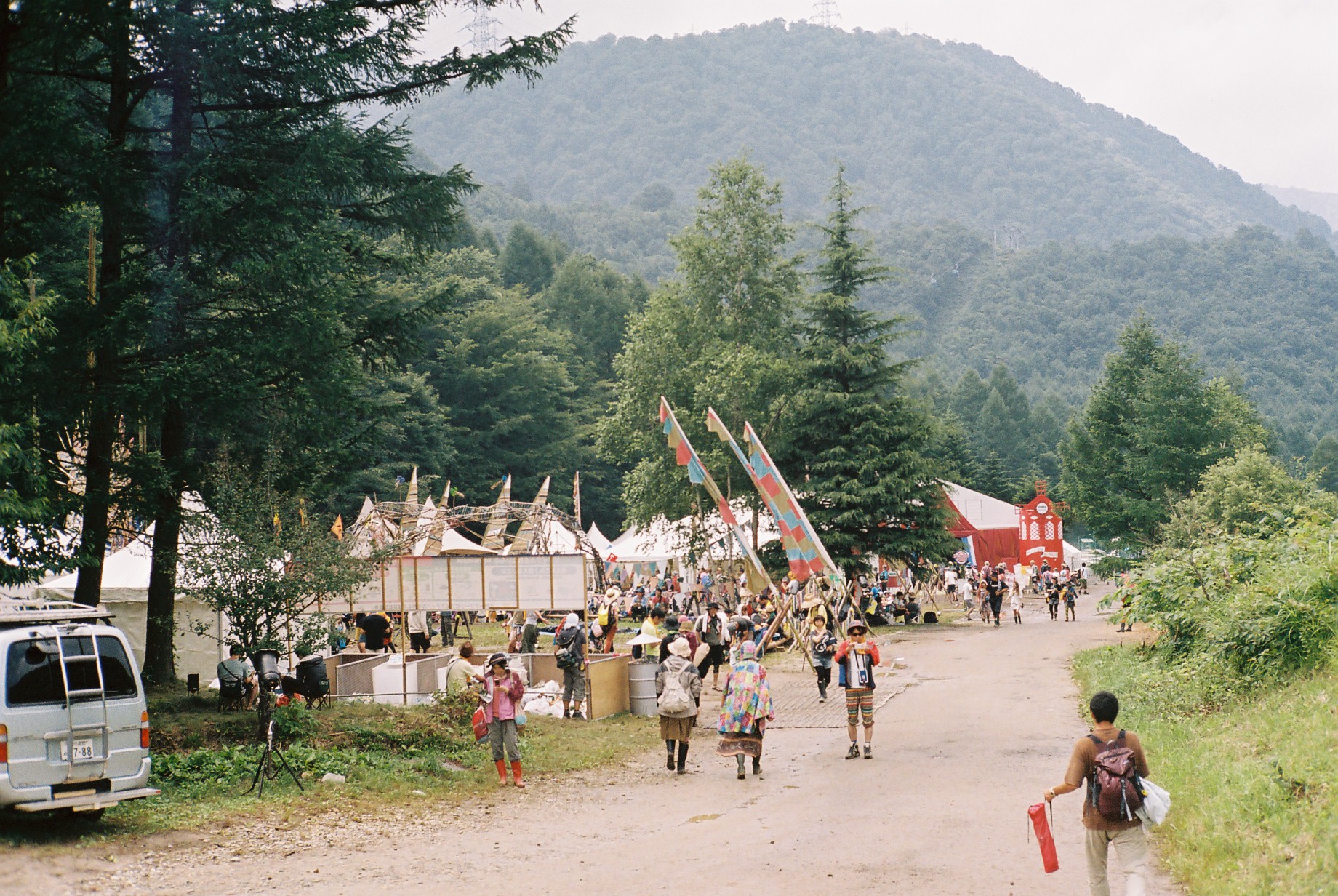 many people walking down a dirt road and flags hanging from the trees