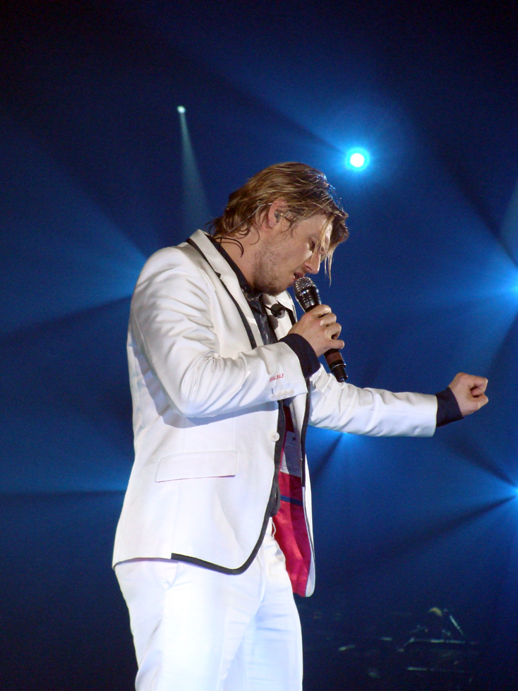 a man wearing a white suit and red tie with a microphone
