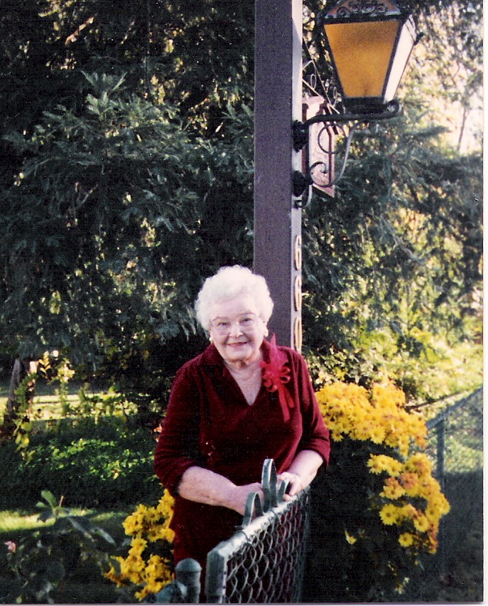 an older woman standing next to a lamp post and flowers