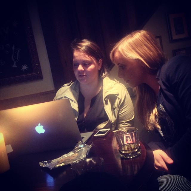 two women sitting next to each other while looking at the screen on a laptop computer