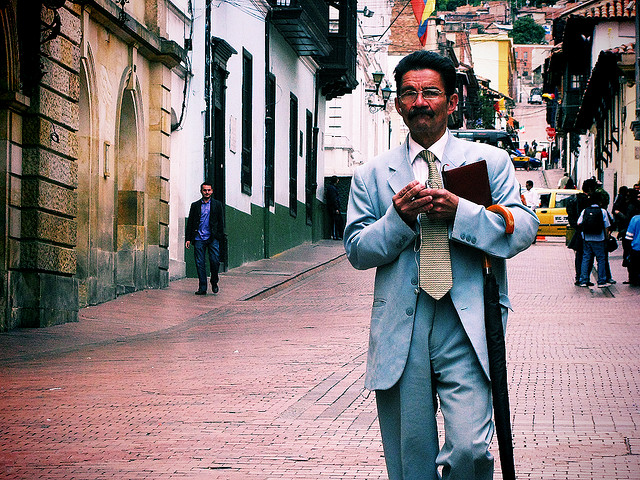 a man wearing glasses holding a book walking down the street