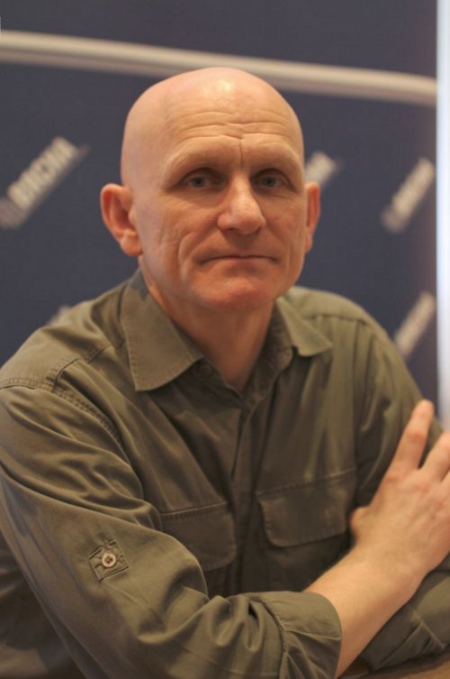 a bald man sitting at a table with his hands folded out