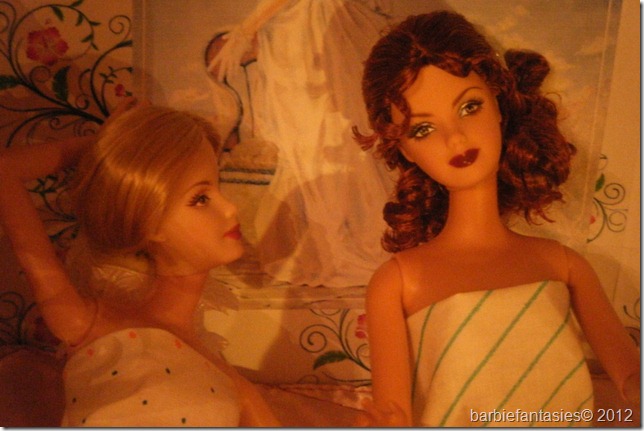 two dolls with very large  in dresses, sitting on a bed