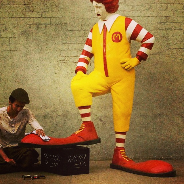 two people kneeling on the ground near a large statue of ronald mcdonald