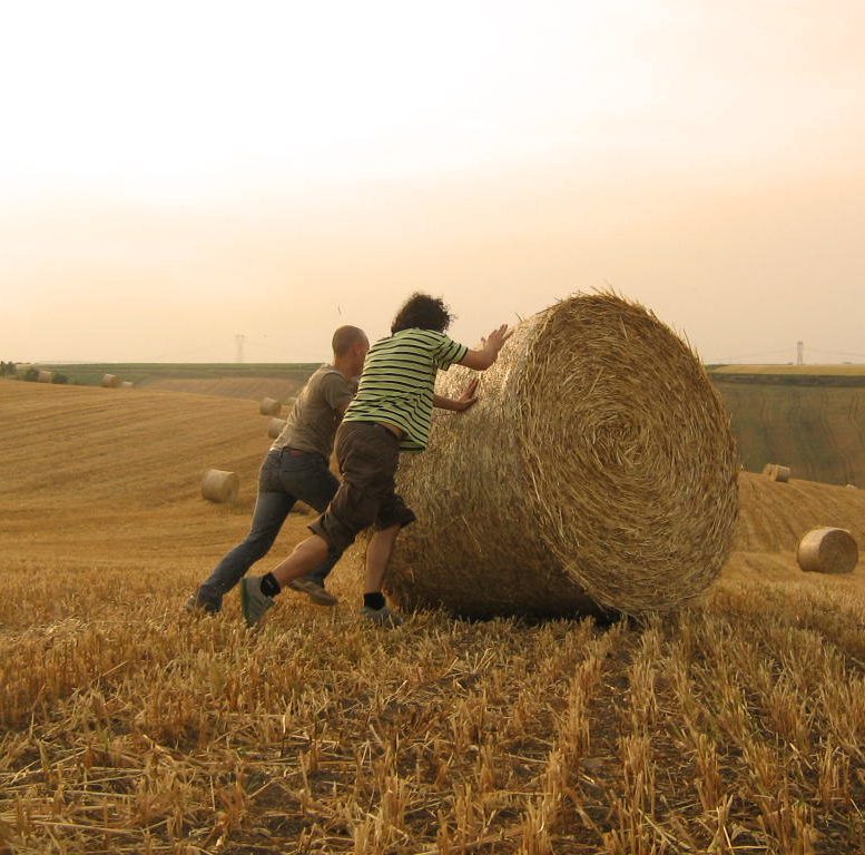 two people climbing up a hay bale on the farm