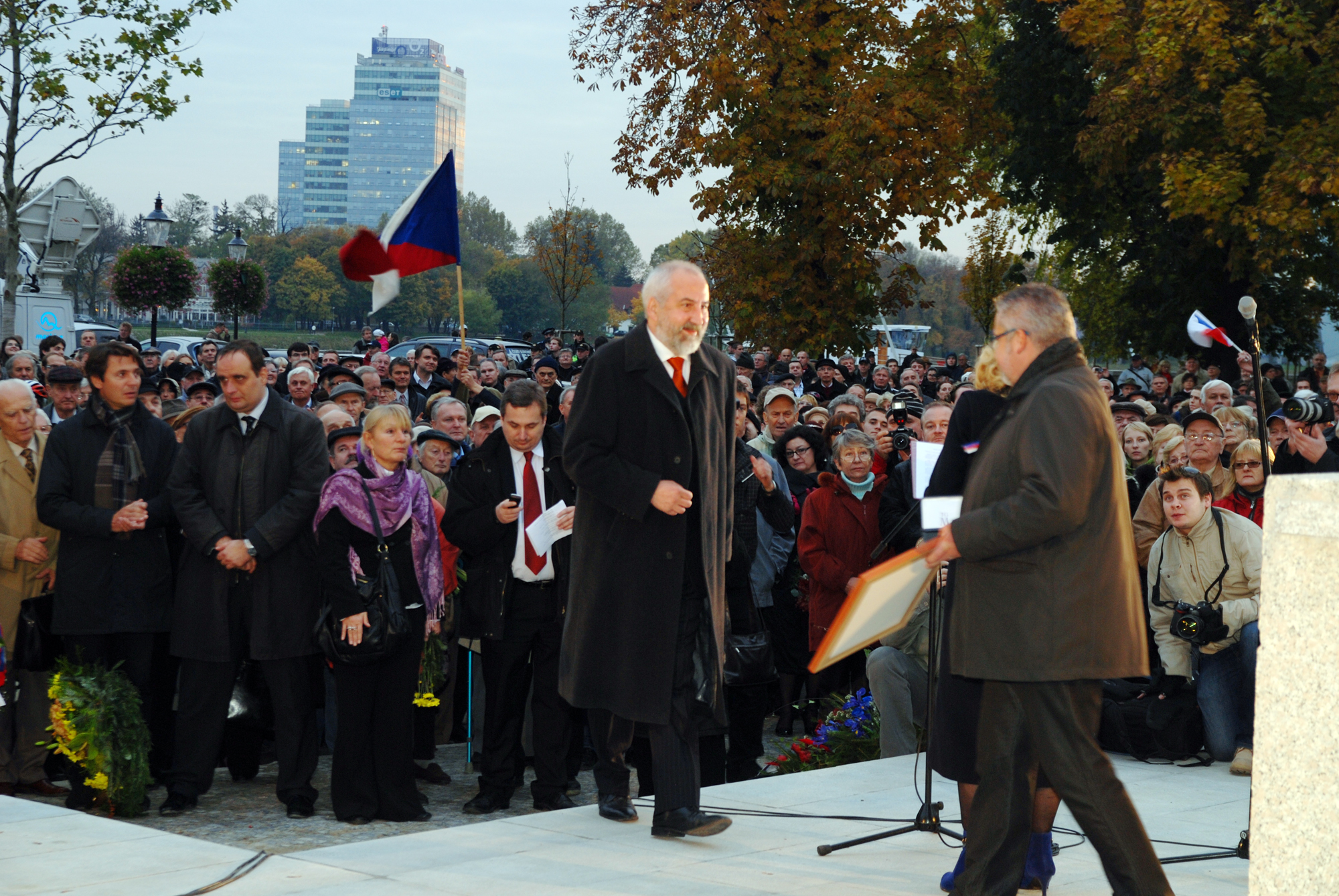there is a man that is at a microphone and another person standing near a flagpole