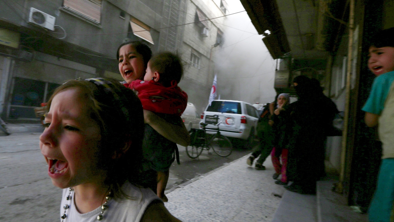 children are standing on the sidewalk near a busy city street