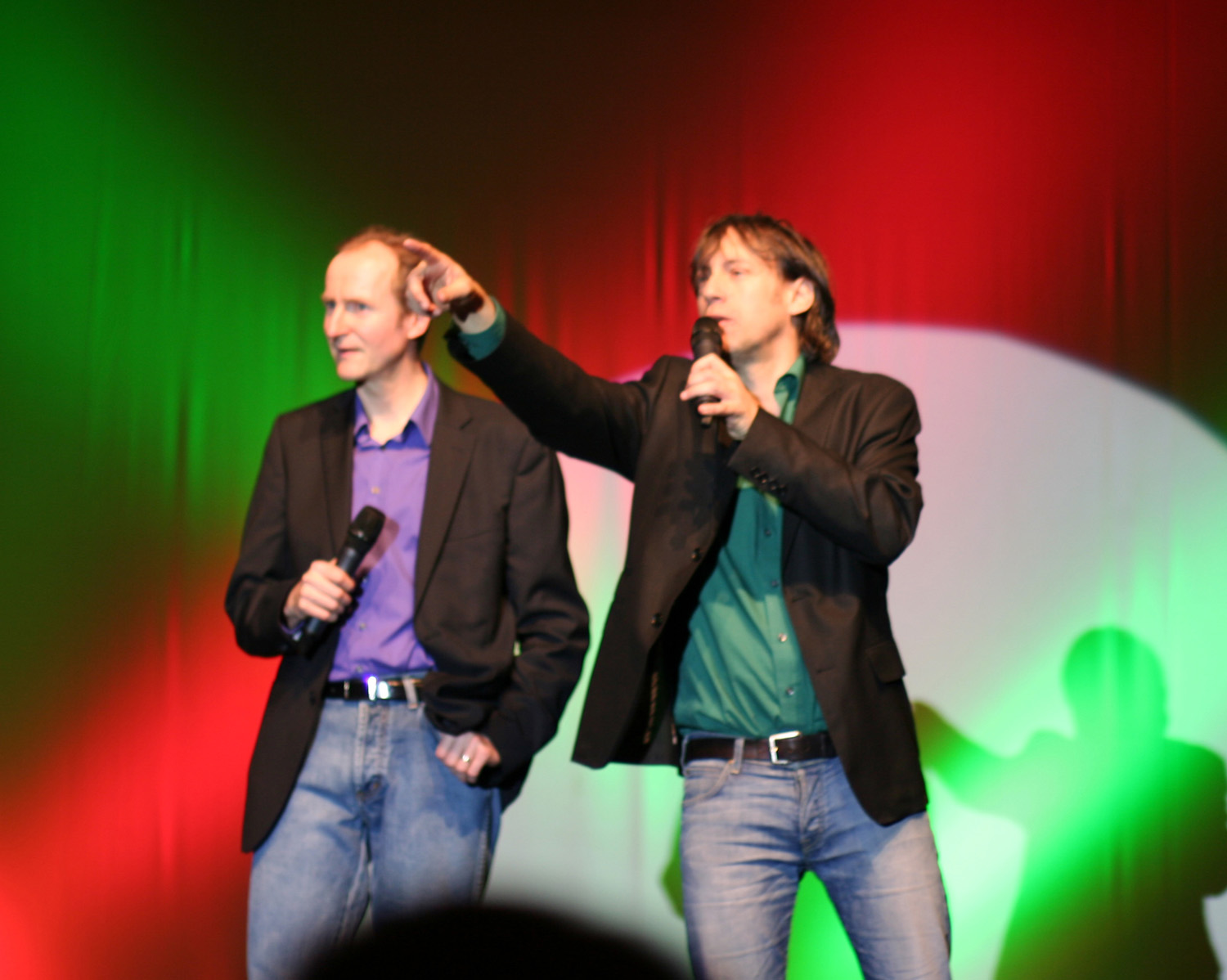 two men standing up with microphones next to each other