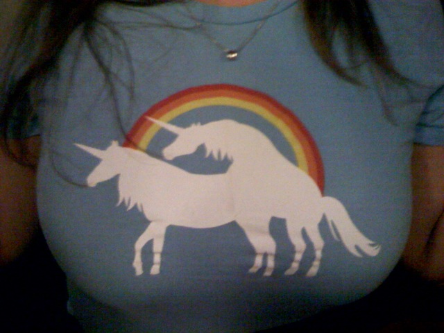 girl wearing a light blue tshirt with white unicorn in front of a rainbow