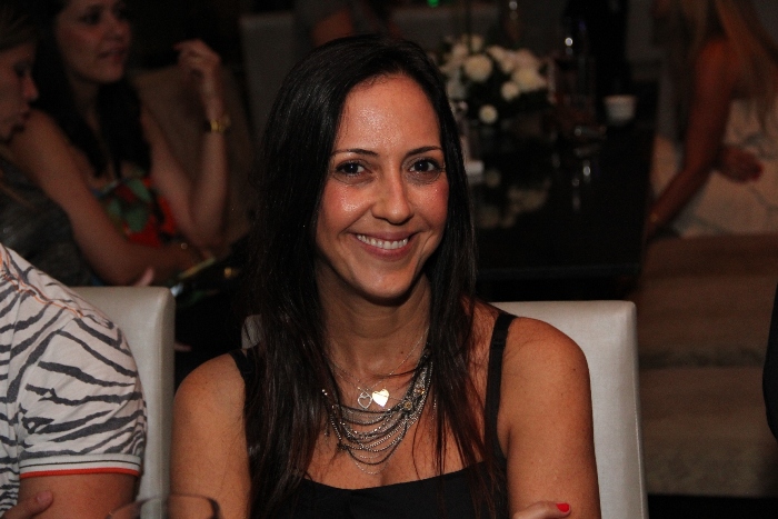a woman sitting at a table smiling while wearing jewelry