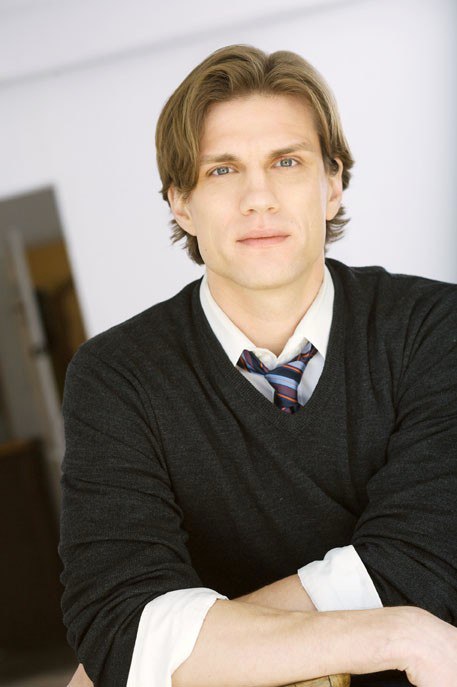 a young man poses for the camera wearing a dark sweater and blue shirt