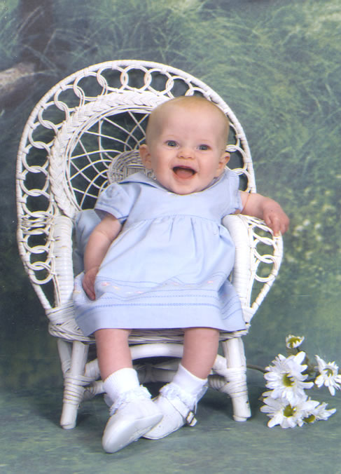 a smiling baby sits in a white wicker chair