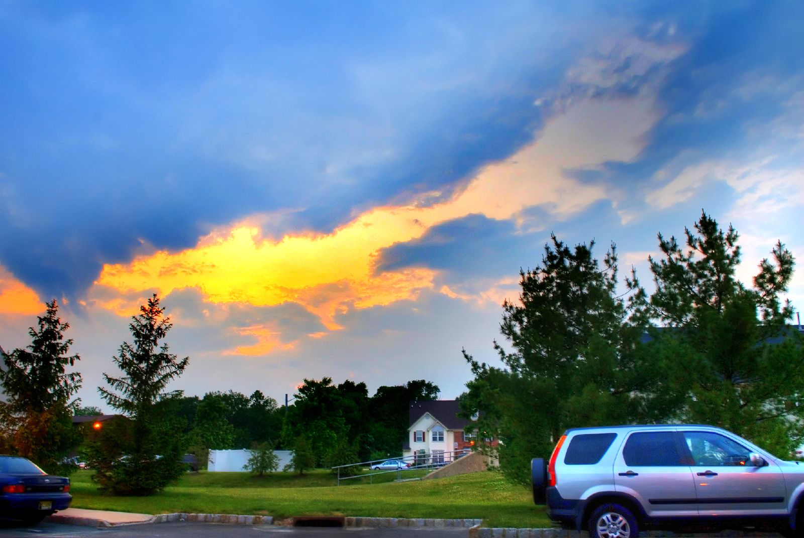 a sunset over a neighborhood with some cars parked in the parking lot