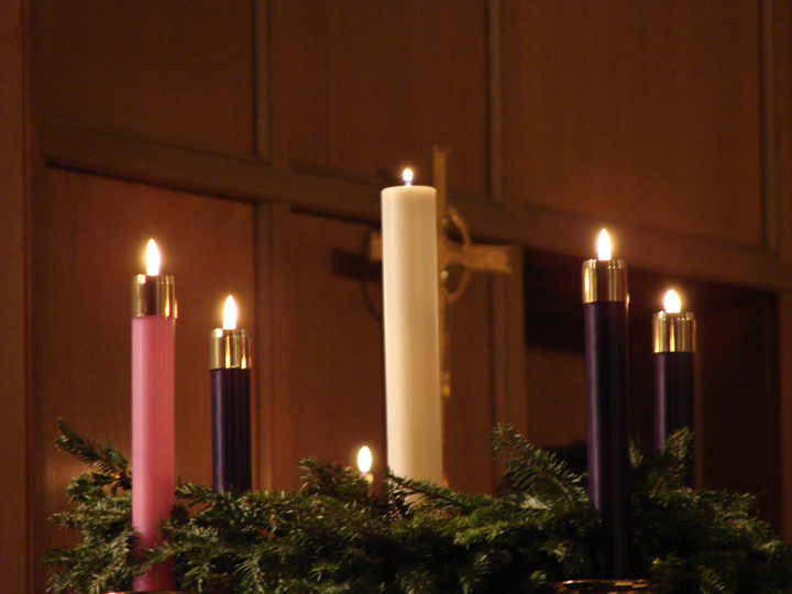 three lit candles with evergreen nches are sitting on a mantle