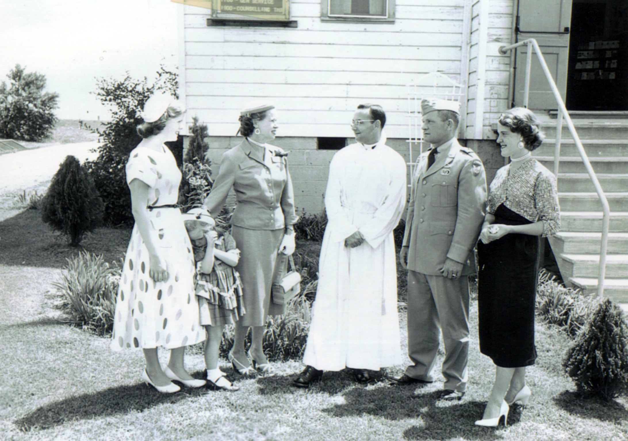 four women and one man are standing in front of a building