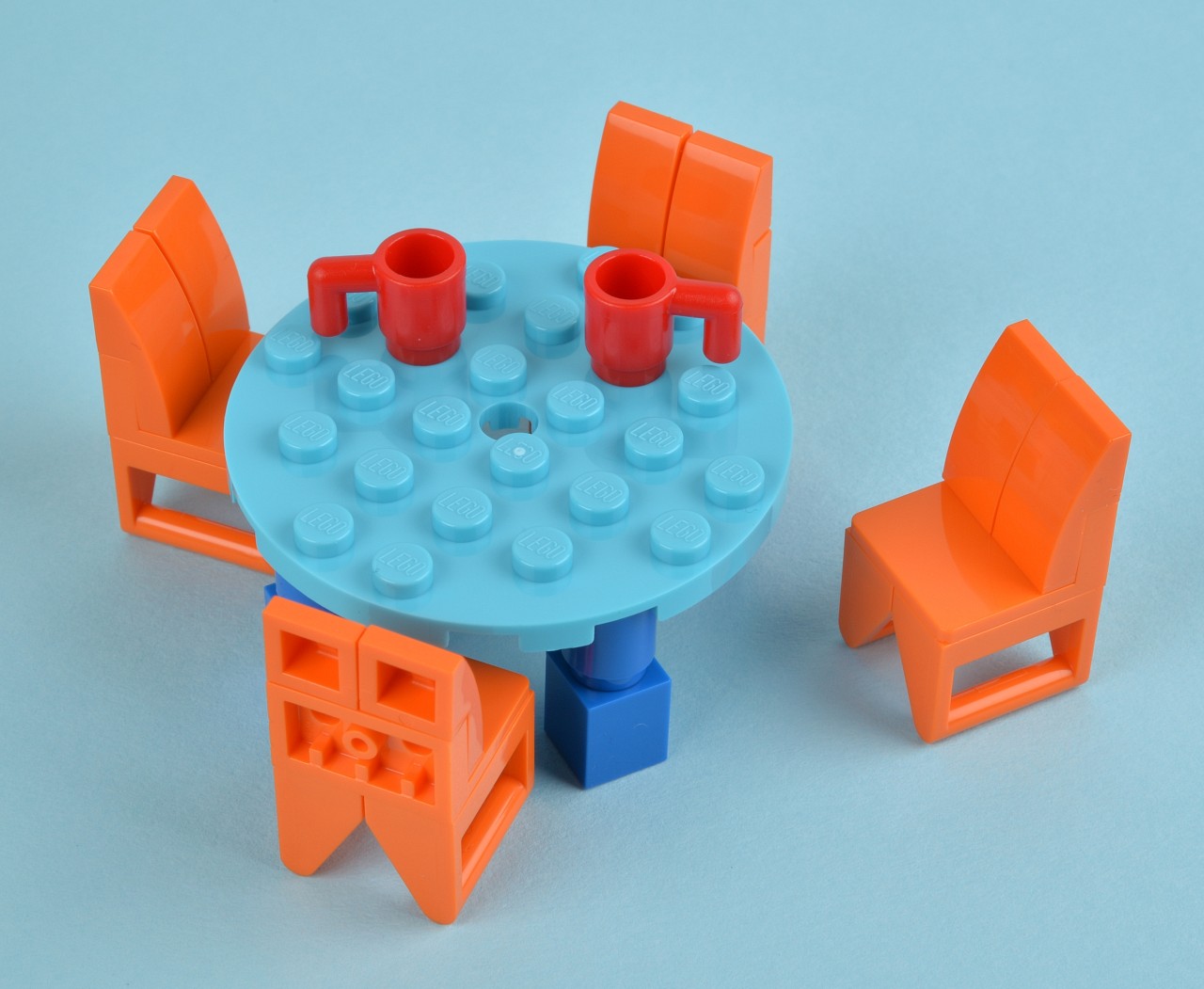 a plastic toy table with four chairs and one table with legos around it