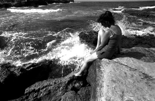 black and white po of woman sitting on rock by ocean