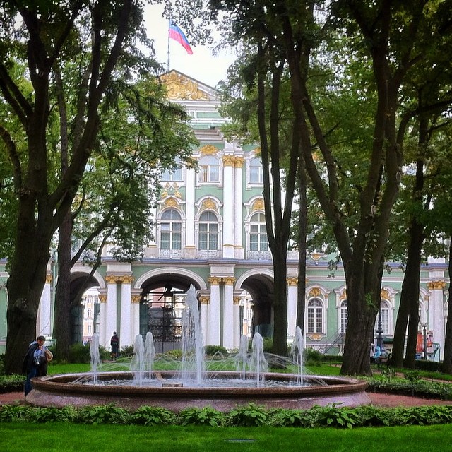 a fountain in front of some trees near many bushes