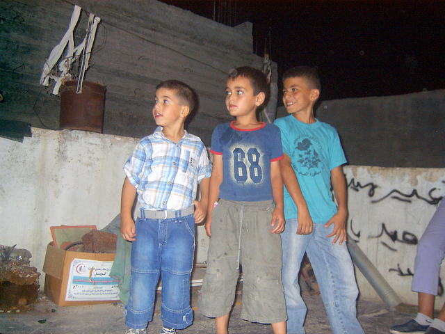three boys stand in the dirt near a wall