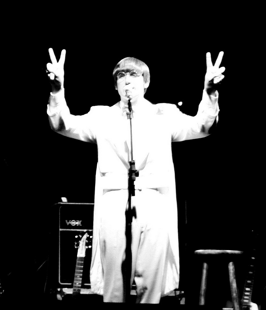 man in white outfit standing on stage singing into a microphone