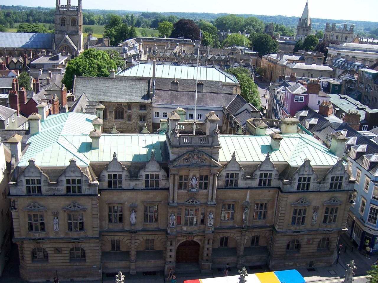 a tall building with many spires, surrounded by buildings and a rainbow colored banner
