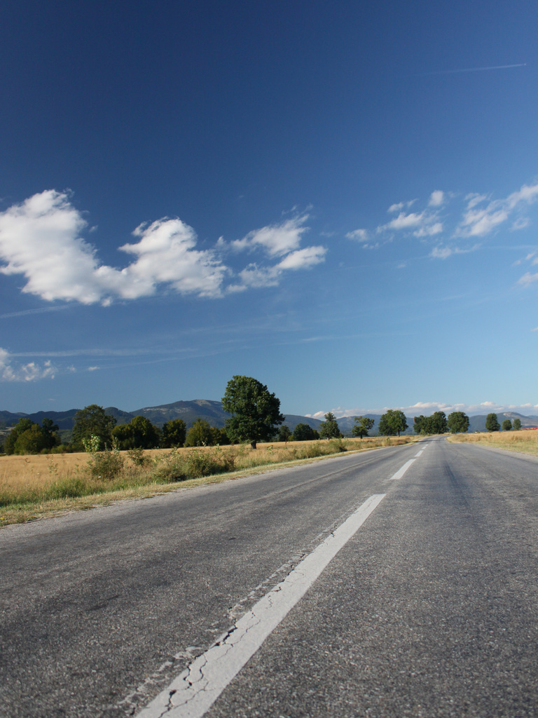 a deserted road in the country with mountains in the distance