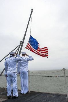 three sailors saluting the flag at an ocean port
