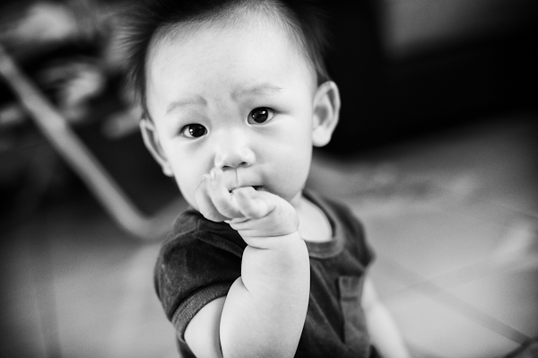 a little asian baby is smiling with the finger in his mouth
