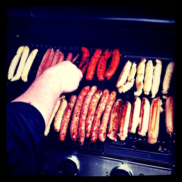 a person putting grilled sausages and  dogs on a grill