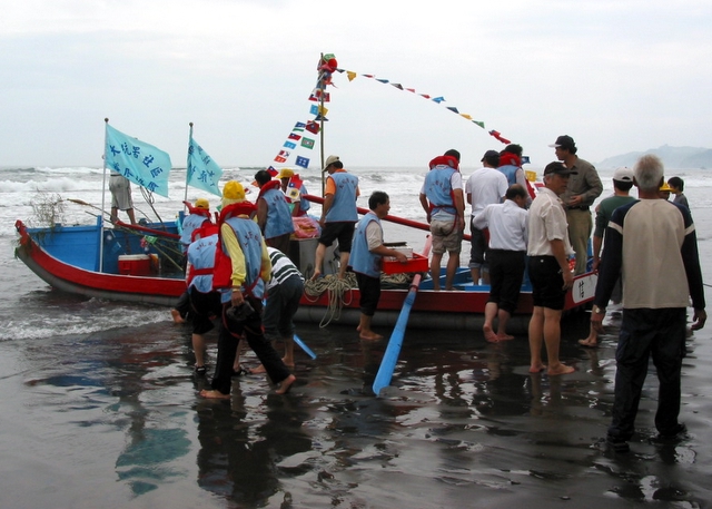 group of people standing next to small boat with flags on beach