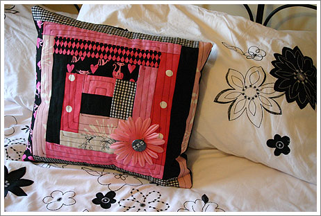 a bed with three pillows, one has a square design and one has a flower in the middle