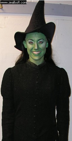a woman in green makeup and black outfit with witches hat